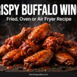Crispy buffalo wings piled on a dark wooden board with glowing embers